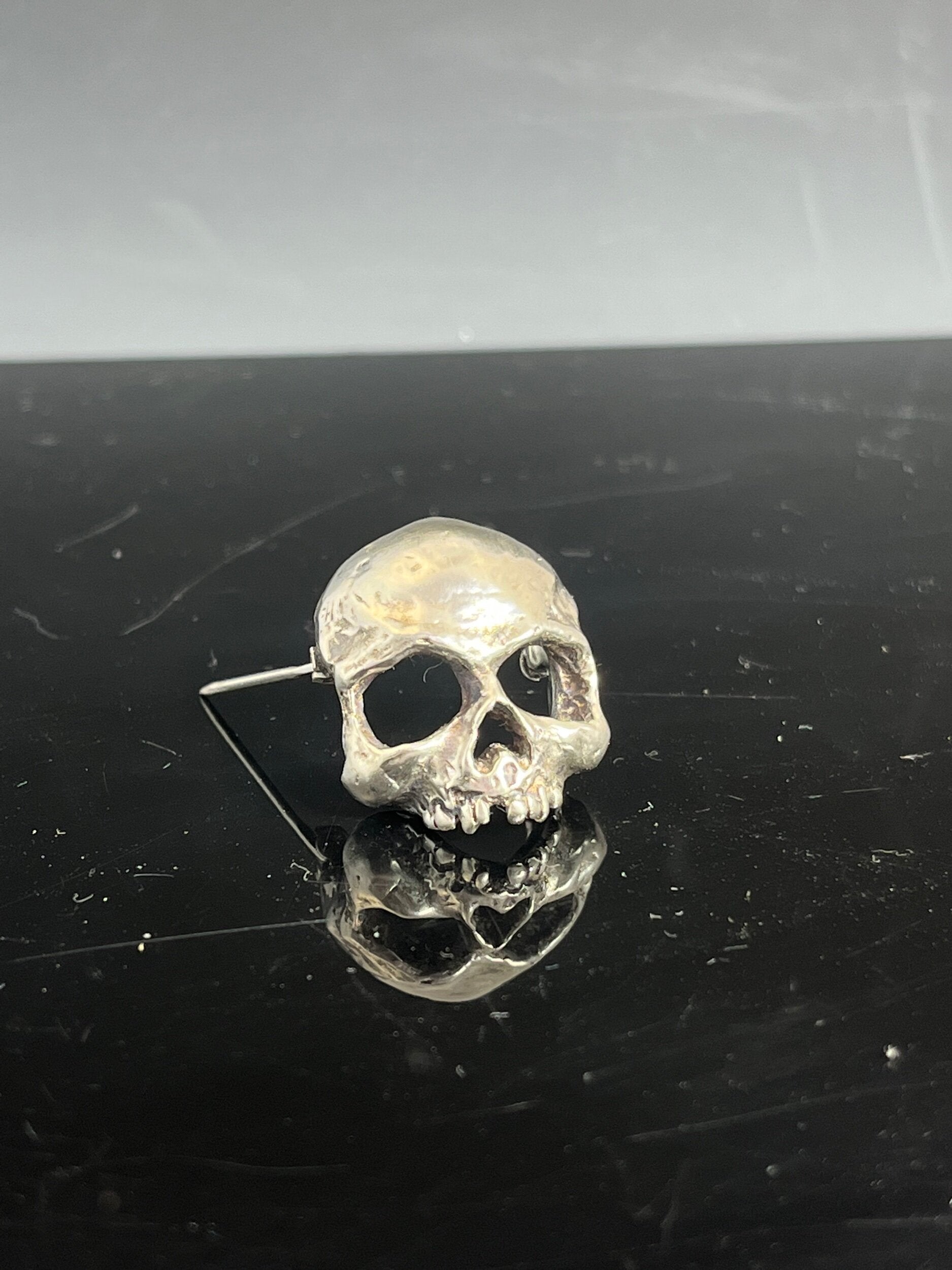 Through the Veil Darkly Skull Face Pin This Through the Veil Darkly Skull Face pin in Sterling Silver has a lot of expression and a nice weight with a hinged pin stem and clasp. It’s not too big or too small or too heavy. It will look great on your sweate