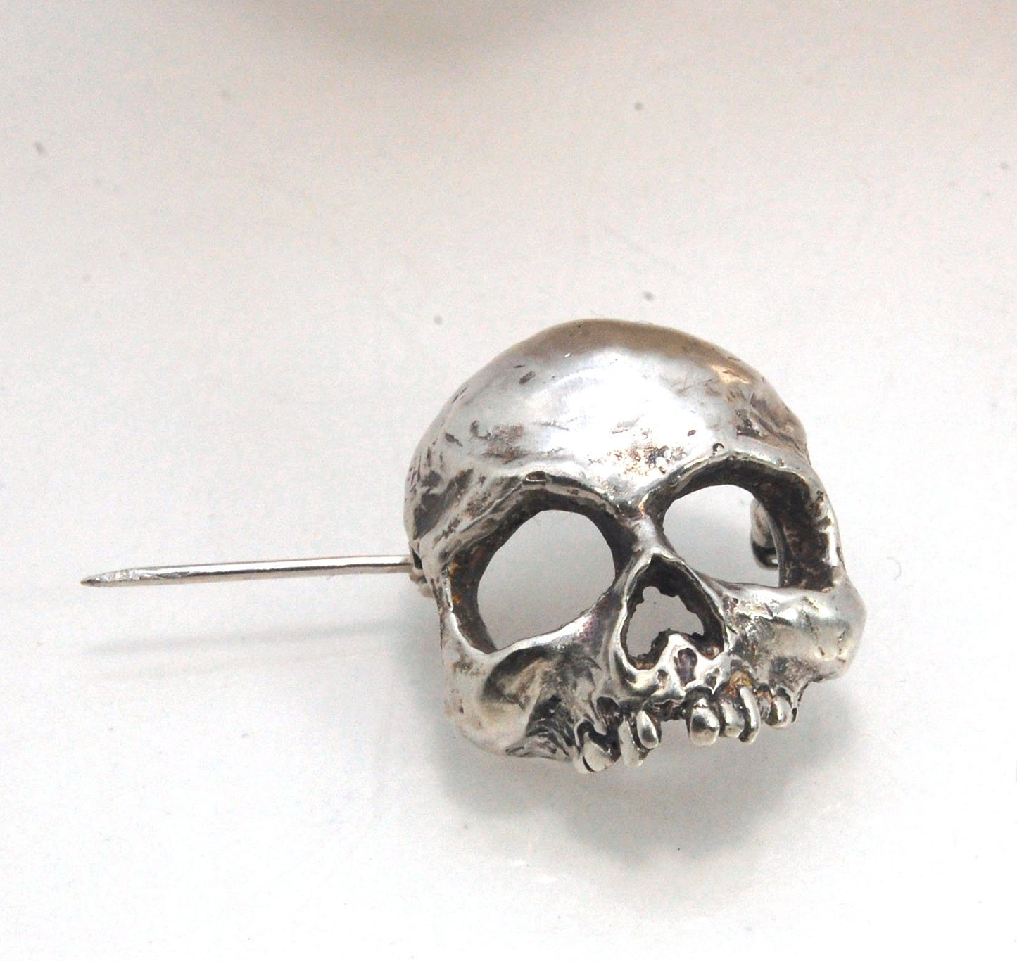 Through the Veil Darkly Skull Face Pin This Through the Veil Darkly Skull Face pin in Sterling Silver has a lot of expression and a nice weight with a hinged pin stem and clasp. It’s not too big or too small or too heavy. It will look great on your sweate