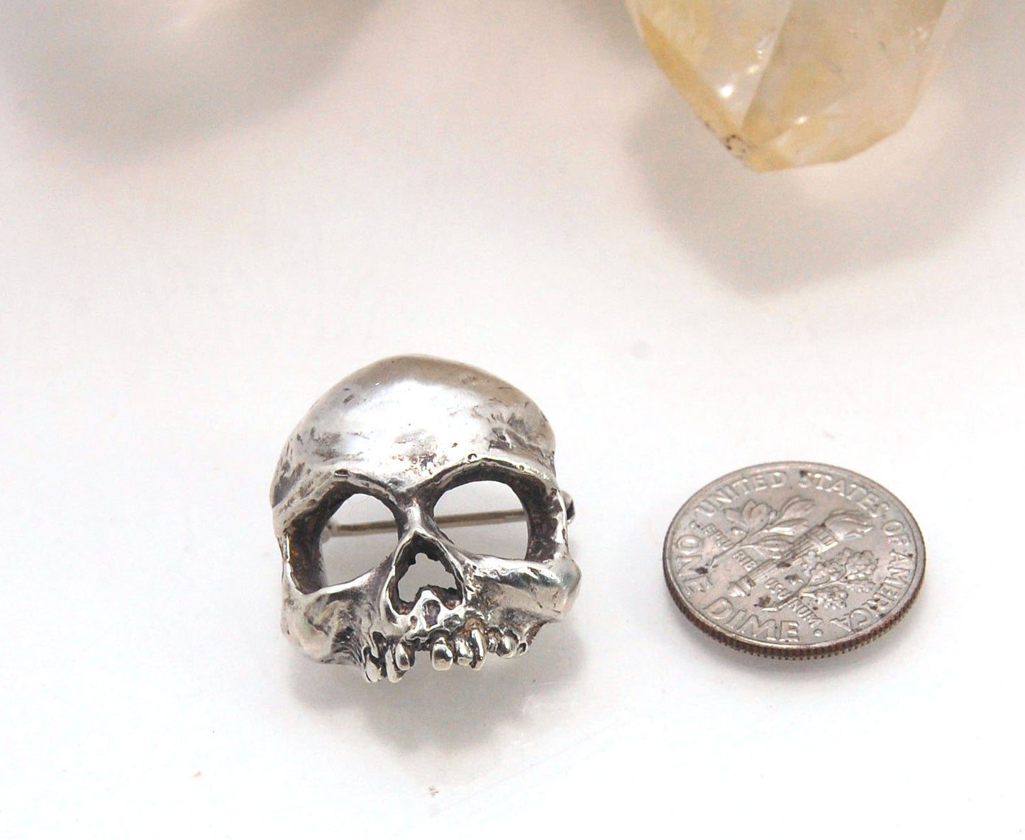 Through the Veil Darkly Skull Face Pin This Through the Veil Darkly Skull Face pin in Sterling Silver has a lot of expression and a nice weight with a hinged pin stem and clasp. It’s not too big or too small or too heavy. It will look great on your sweate