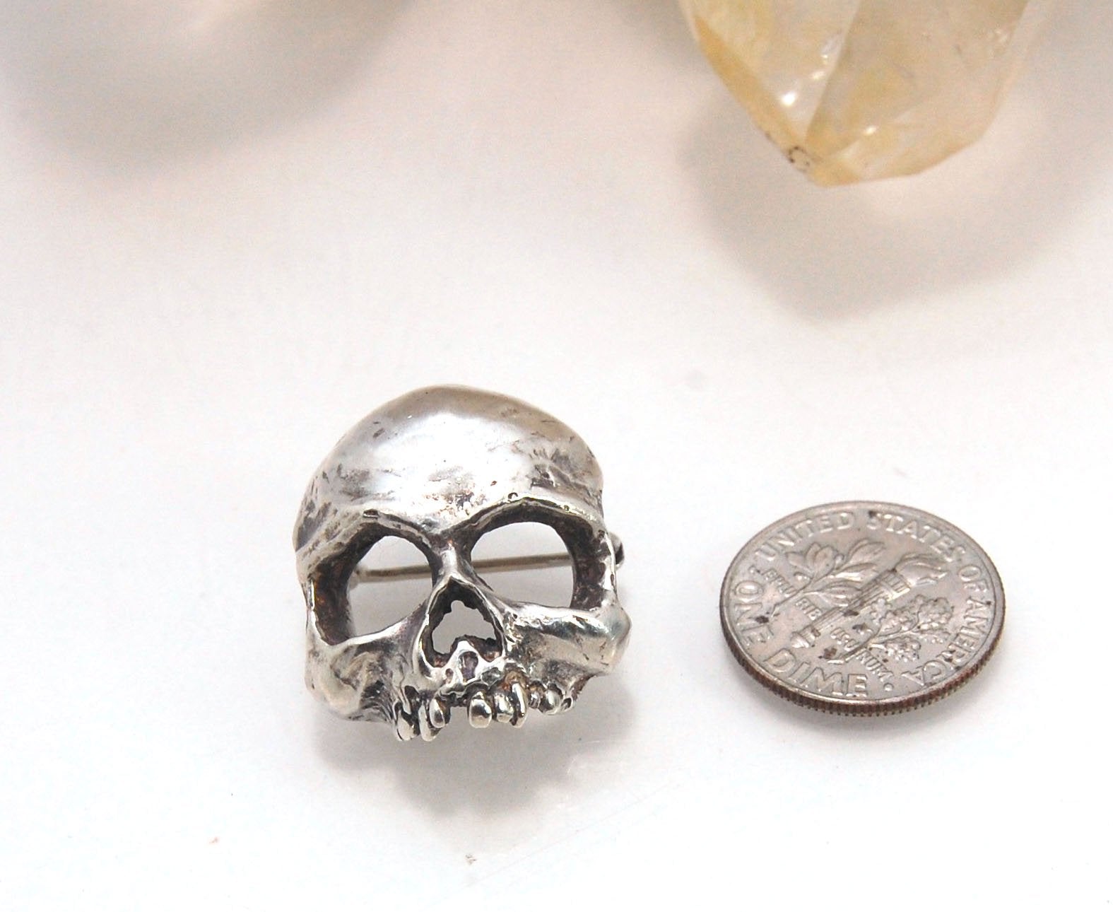 Through the Veil Darkly Skull Face Pin This Through the Veil Darkly Skull Face pin in Sterling Silver has a lot of expression and a nice weight with a hinged pin stem and clasp. It’s not too big or too small or too heavy. It will look great on your sweate