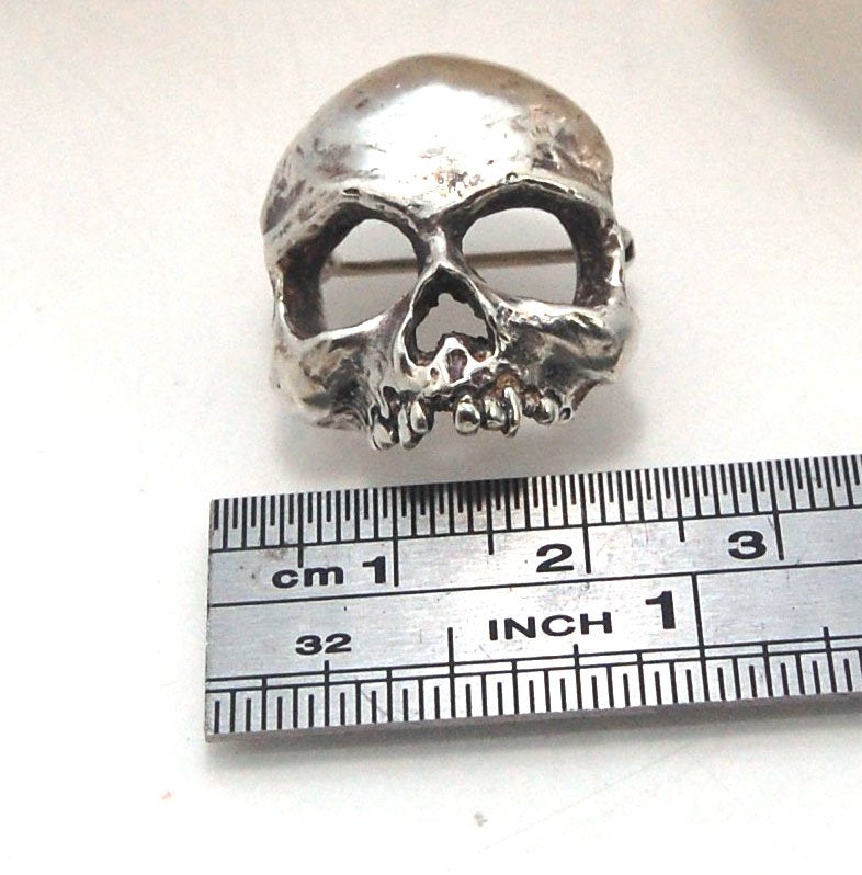 Through the Veil Darkly Skull Face Pin This Through the Veil Darkly Skull Face pin in Sterling Silver has a lot of expression and a nice weight with a hinged pin stem and clasp. It’s not too big or too small or too heavy. It will look great on your sweate