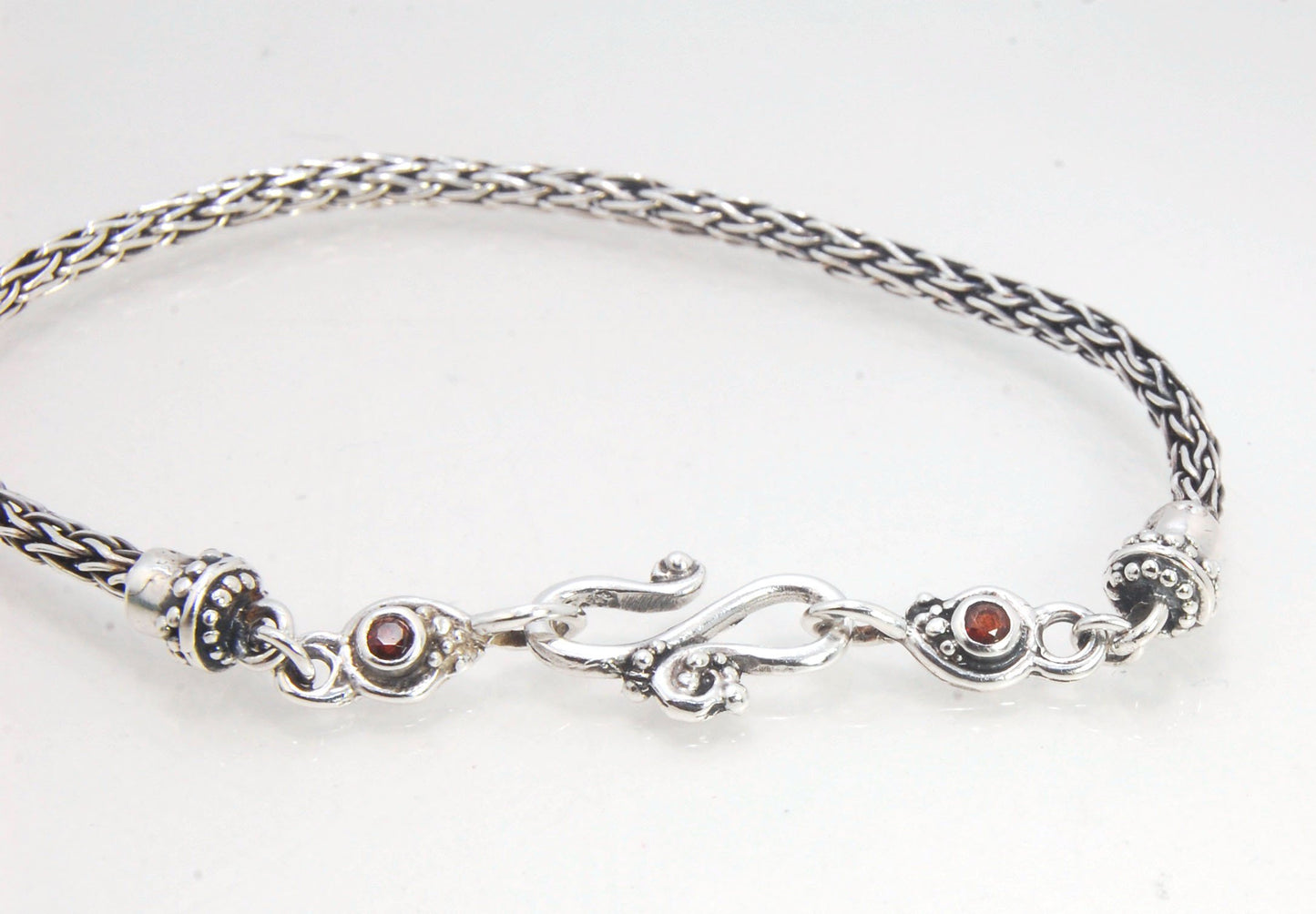 Garnet Wisteria Viking Knit Woven Silver Bracelet These woven bracelets are hand-woven in Viking knit style from fine silver with a cast granulated cap, garnet set Wisteria settings and a sterling S clasp. This chain takes many hours to make. The original