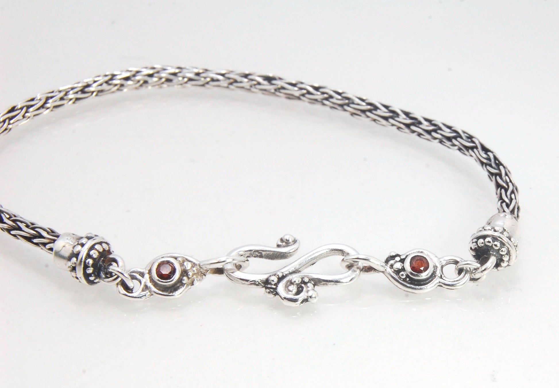 Garnet Wisteria Viking Knit Woven Silver Bracelet These woven bracelets are hand-woven in Viking knit style from fine silver with a cast granulated cap, garnet set Wisteria settings and a sterling S clasp. This chain takes many hours to make. The original