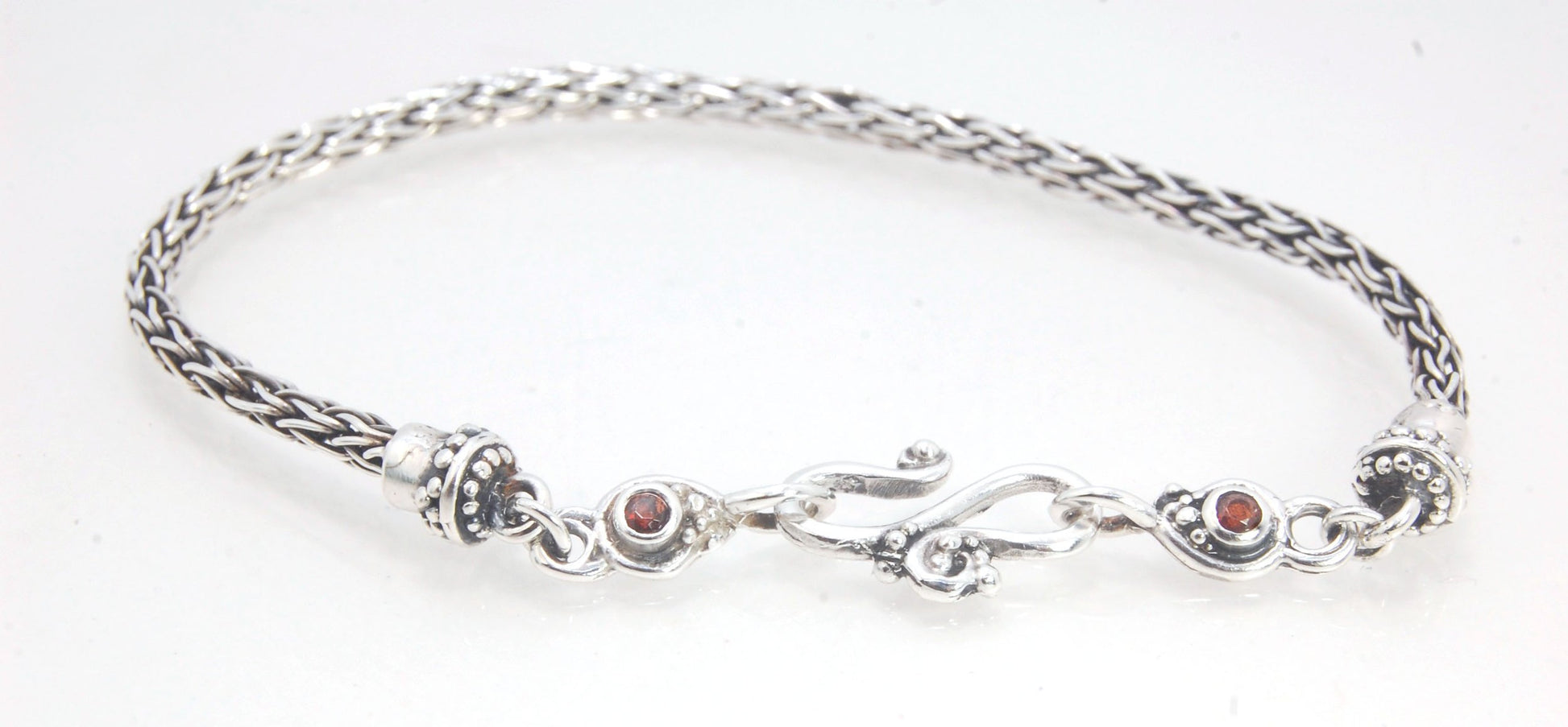 Garnet Wisteria Viking Knit Woven Silver Bracelet These woven bracelets are hand-woven in Viking knit style from fine silver with a cast granulated cap, garnet set Wisteria settings and a sterling S clasp. This chain takes many hours to make. The original