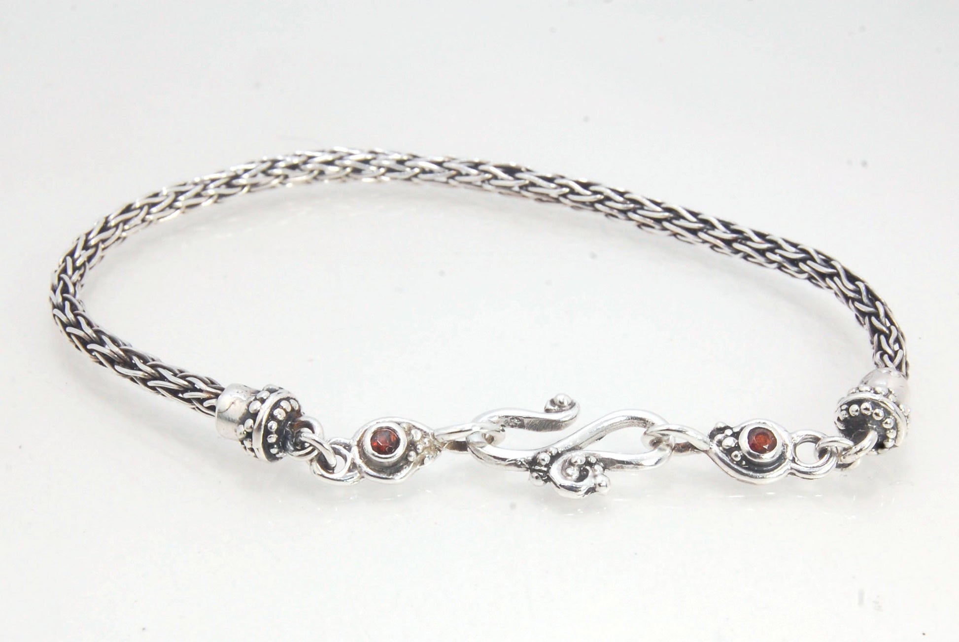 Garnet Wisteria Viking Knit Woven Silver Bracelet These woven bracelets are hand-woven in Viking knit style from fine silver with a cast granulated cap, garnet set Wisteria settings and a sterling S clasp. This chain takes many hours to make. The original