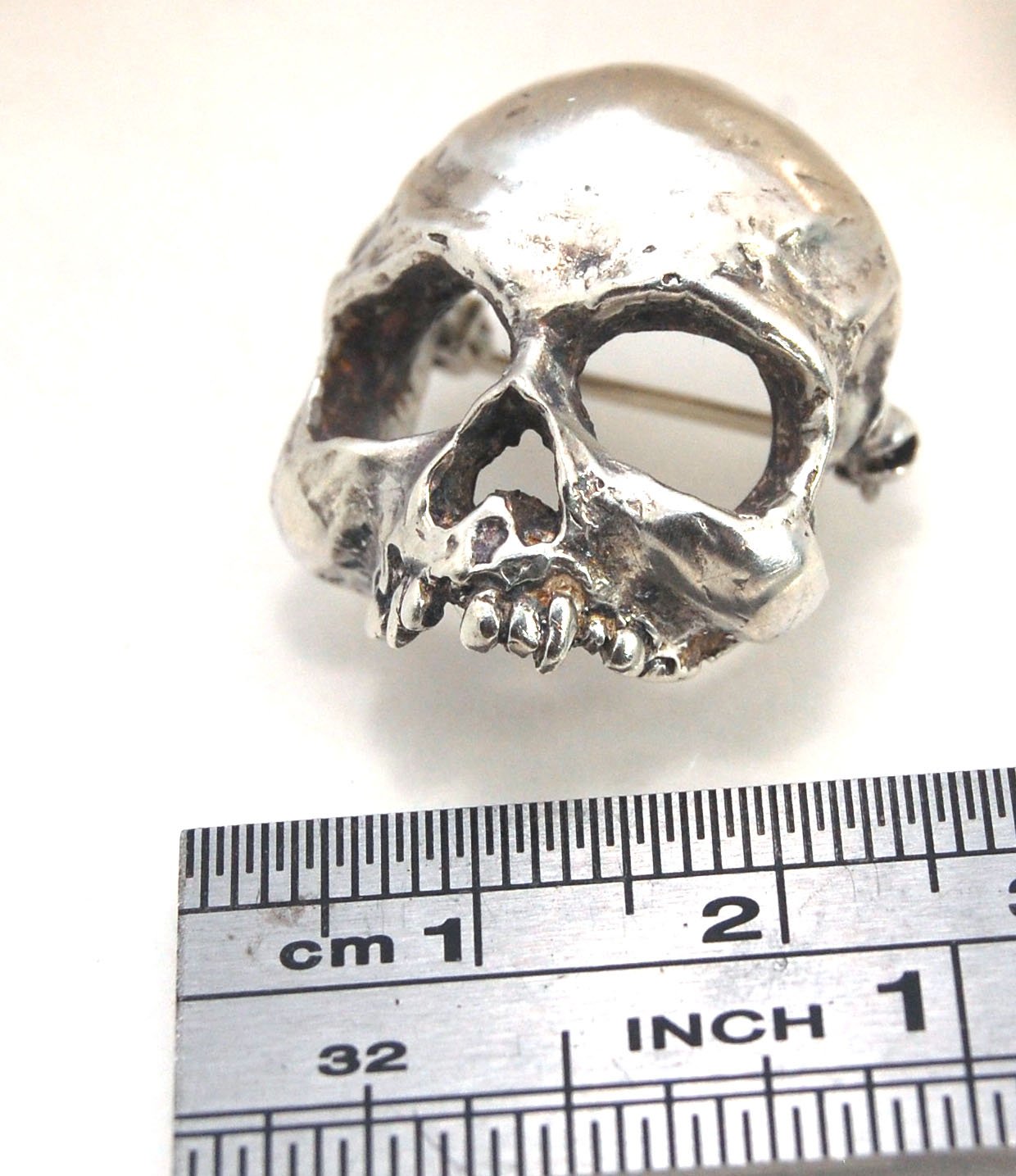Through the Veil Darkly Skull Face Pin This Through the Veil Darkly Skull Face pin in Sterling Silver has a lot of expression and a nice weight with a hinged pin stem and clasp. It’s not too big or too small or too heavy. It will look great on your sweate