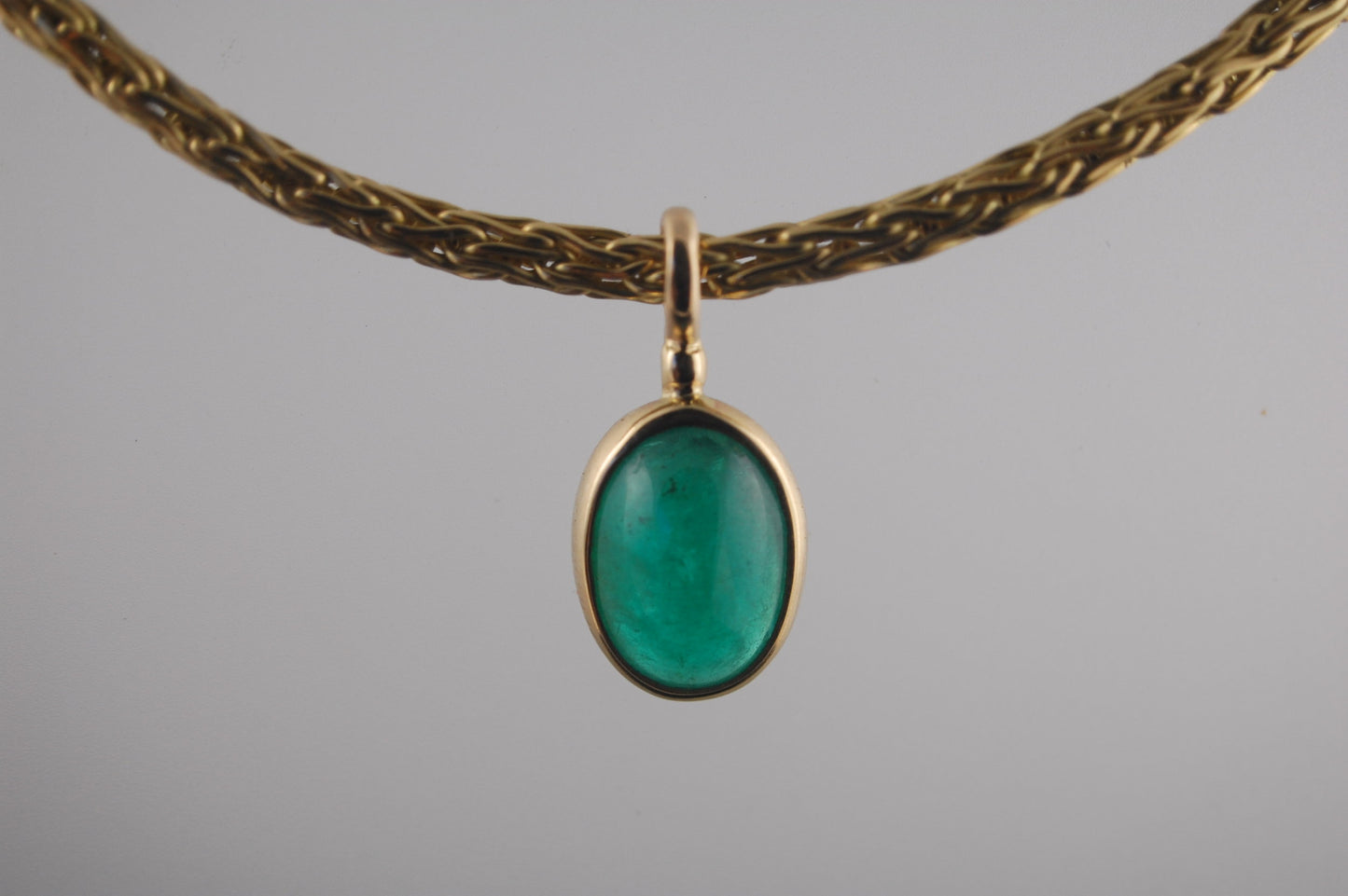 Emerald Cabochon on Handmade Woven 18k gold chain This clear emerald cabochon is bezel-set in 18k gold and suspended from a handmade woven chain of 18k gold in ancient Viking knit. A forged hook clasp finishes this simple and elegant design. Emerald Caboc