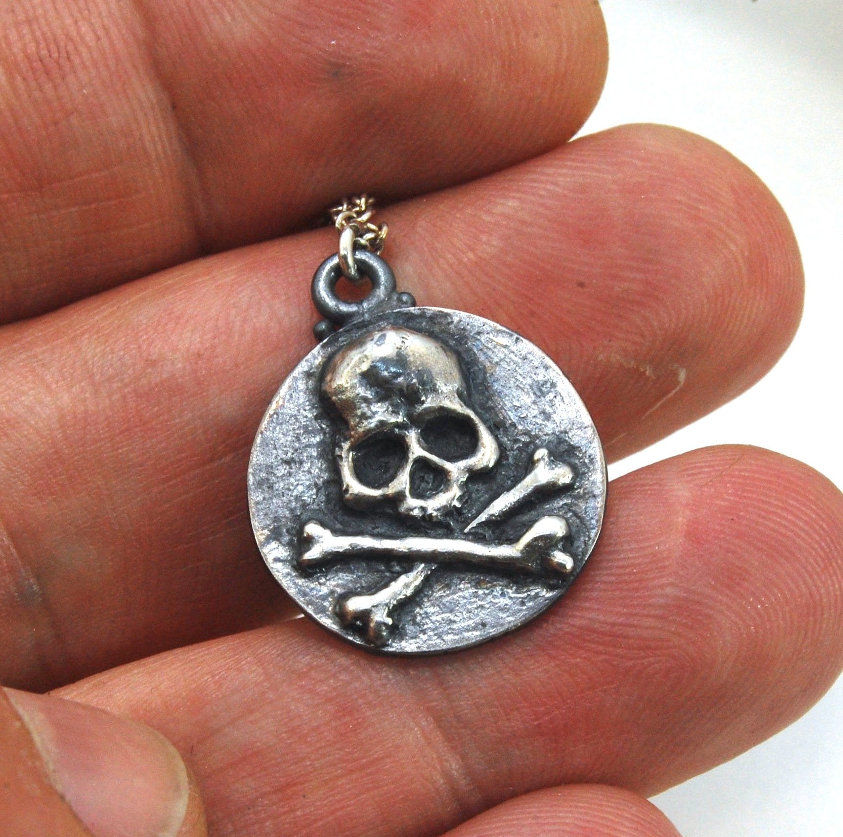 Skullbones Coin Pendant This solid sterling silver Skulbones coin pendant is wax carved by hand and cast using the ancient process of Lost Wax casting. I then made a mold, which I can inject with wax and make wax copies of the Skull and Crossbones Coin an