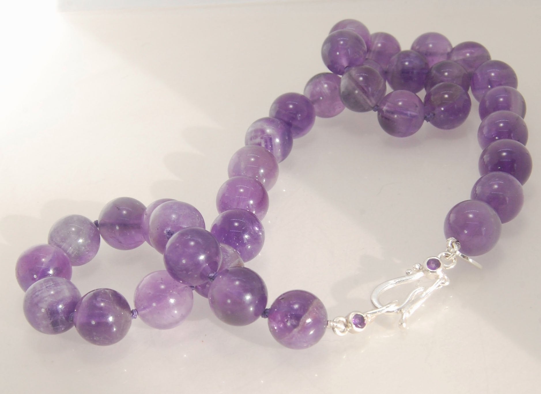 Round Amethyst Gemstone Knotted Strand These lovely round Amethyst Gemstone Beads are a large 11.5mm! These beauties have a nice weight and warmth and are knotted on silk like pearls. I have made a sterling silver two-part clasp with faceted amethysts and