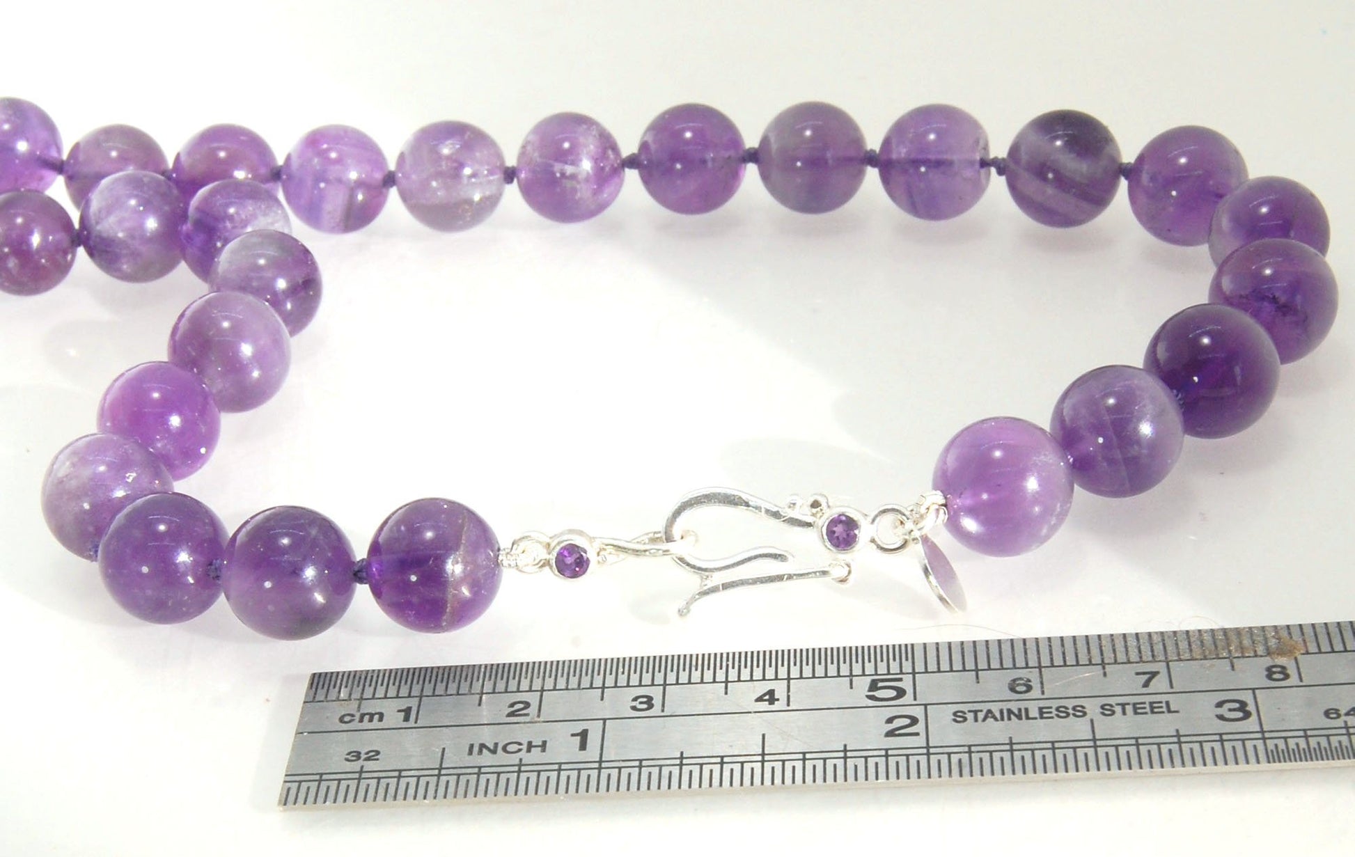 Round Amethyst Gemstone Knotted Strand These lovely round Amethyst Gemstone Beads are a large 11.5mm! These beauties have a nice weight and warmth and are knotted on silk like pearls. I have made a sterling silver two-part clasp with faceted amethysts and