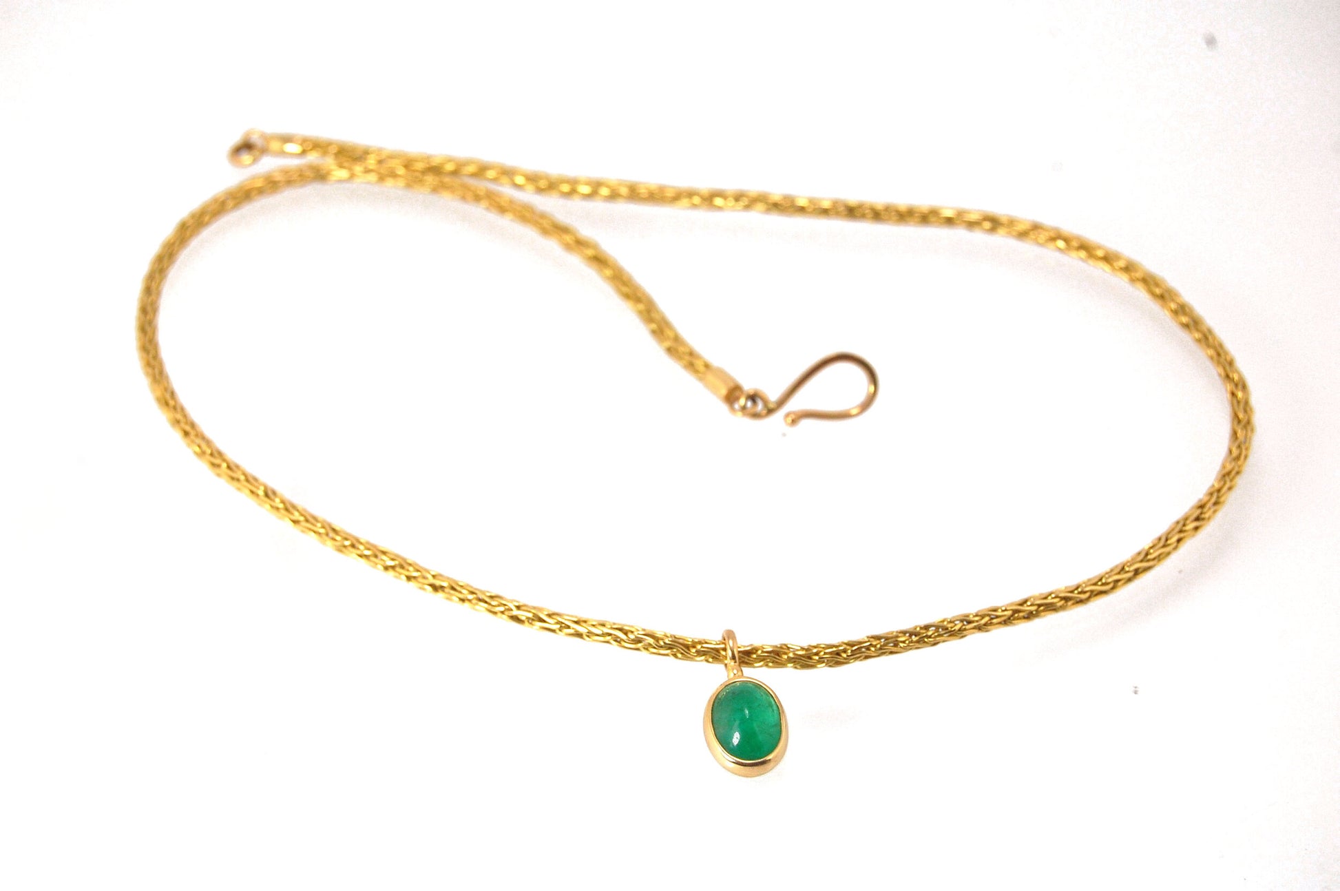 Emerald Cabochon on Handmade Woven 18k gold chain This clear emerald cabochon is bezel-set in 18k gold and suspended from a handmade woven chain of 18k gold in ancient Viking knit. A forged hook clasp finishes this simple and elegant design. Emerald Caboc