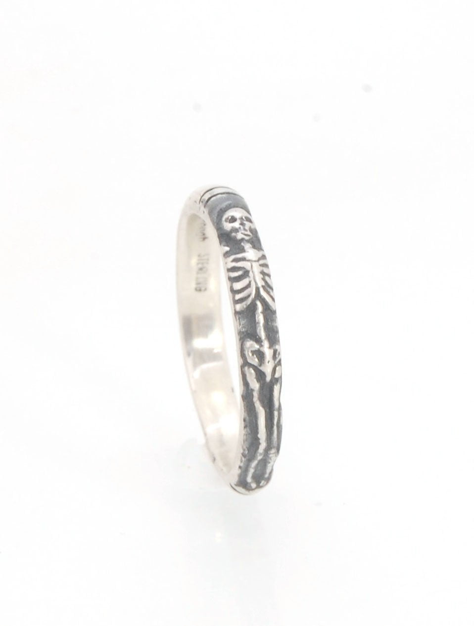 Oxidized Memento Mori Skeleton Ring - 3.3mm - Sterling silver This is the second-most narrow of my Memento Mori rings at 3.3mm wide. This is the cute skeleton with the shy knees! The Skeleton is flanked by intertwined hearts on one side and about 1/2 of t