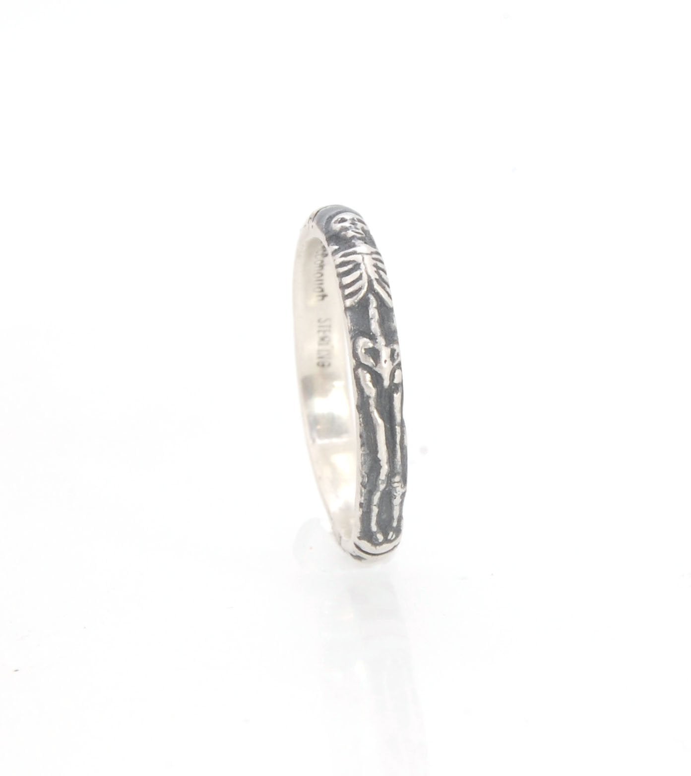 Oxidized Memento Mori Skeleton Ring - 3.3mm - Sterling silver This is the second-most narrow of my Memento Mori rings at 3.3mm wide. This is the cute skeleton with the shy knees! The Skeleton is flanked by intertwined hearts on one side and about 1/2 of t