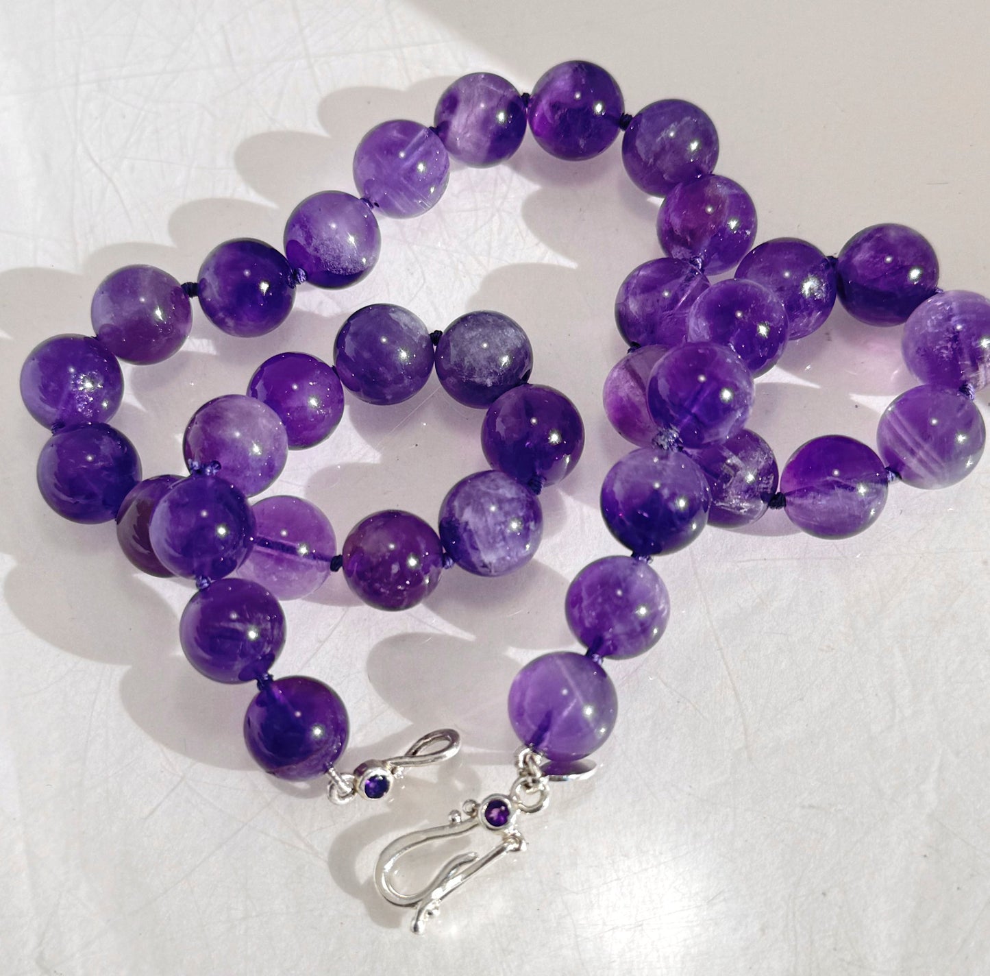 Round Amethyst Gemstone Knotted Strand These lovely round Amethyst Gemstone Beads are a large 11.5mm! These beauties have a nice weight and warmth and are knotted on silk like pearls. I have made a sterling silver two-part clasp with faceted amethysts and