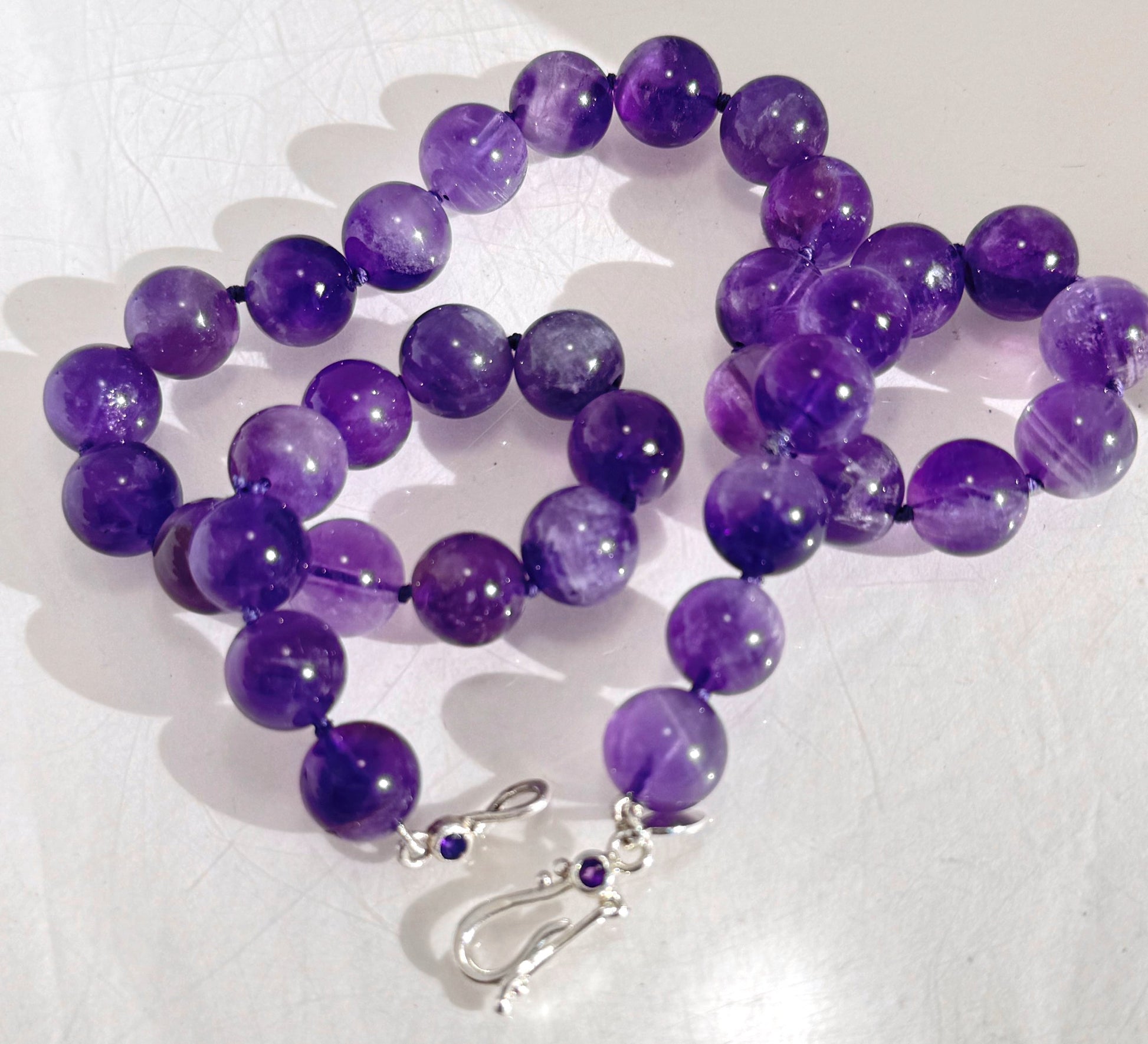 Round Amethyst Gemstone Knotted Strand These lovely round Amethyst Gemstone Beads are a large 11.5mm! These beauties have a nice weight and warmth and are knotted on silk like pearls. I have made a sterling silver two-part clasp with faceted amethysts and