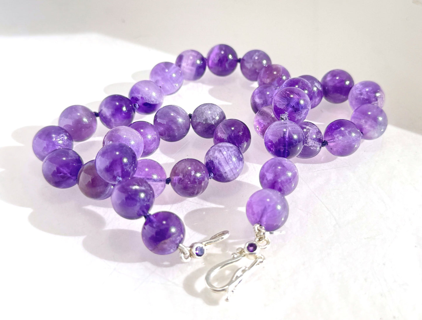 Round Amethyst Gemstone Knotted Strand These lovely round Amethyst Gemstone Beads are a large 11.5mm! These beauties have a nice weight and warmth and are knotted on silk like pearls. I have made a sterling silver two-part clasp with faceted amethysts and