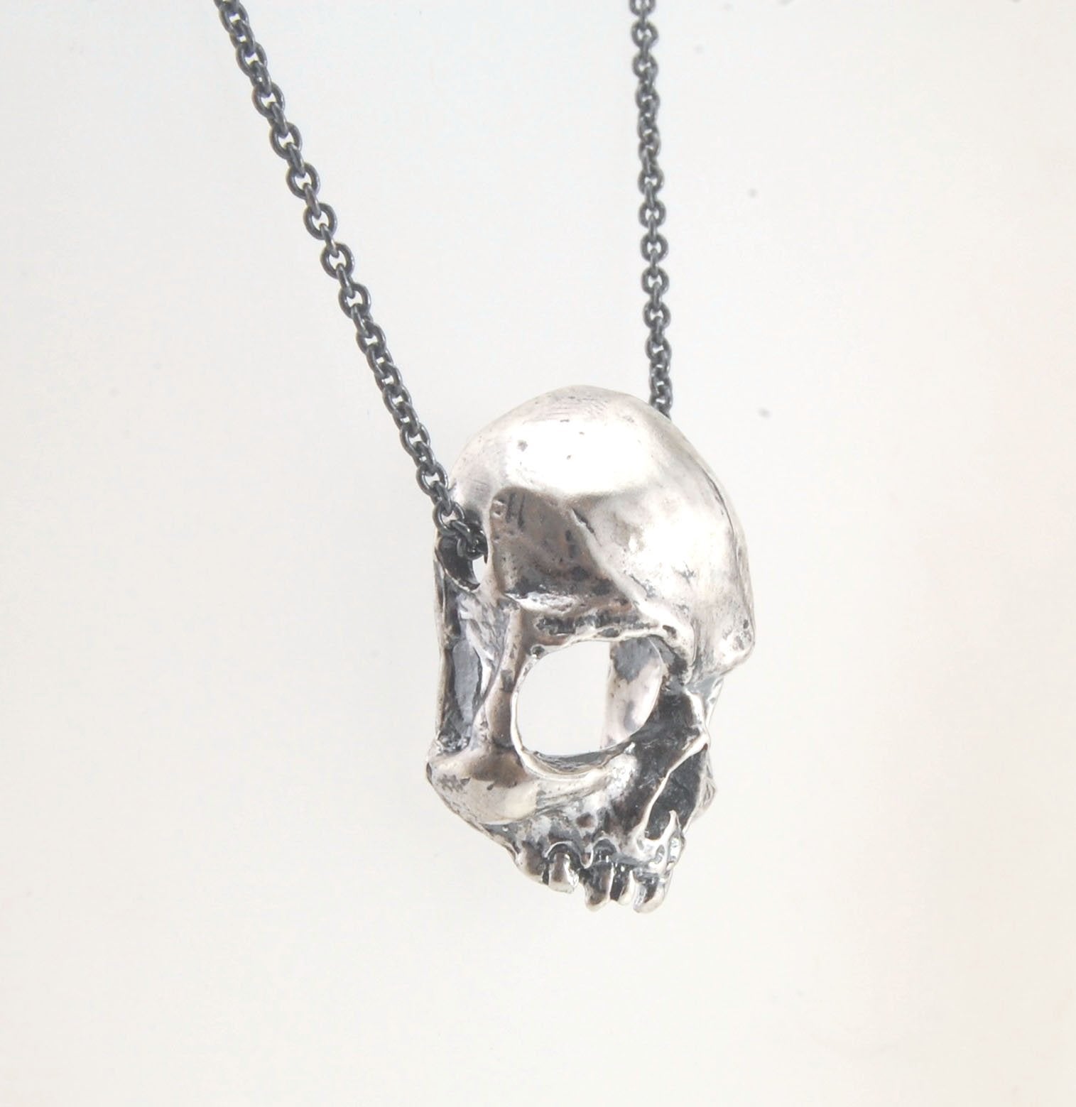 Through the Veil Darkly Skull Face Slider Necklace This Through the Veil Darkly Skull Face pendant in Sterling Silver has a lot of expression and a nice weight with an oxidized sterling silver chain passing thorugh the back of the face. It’s not too big o