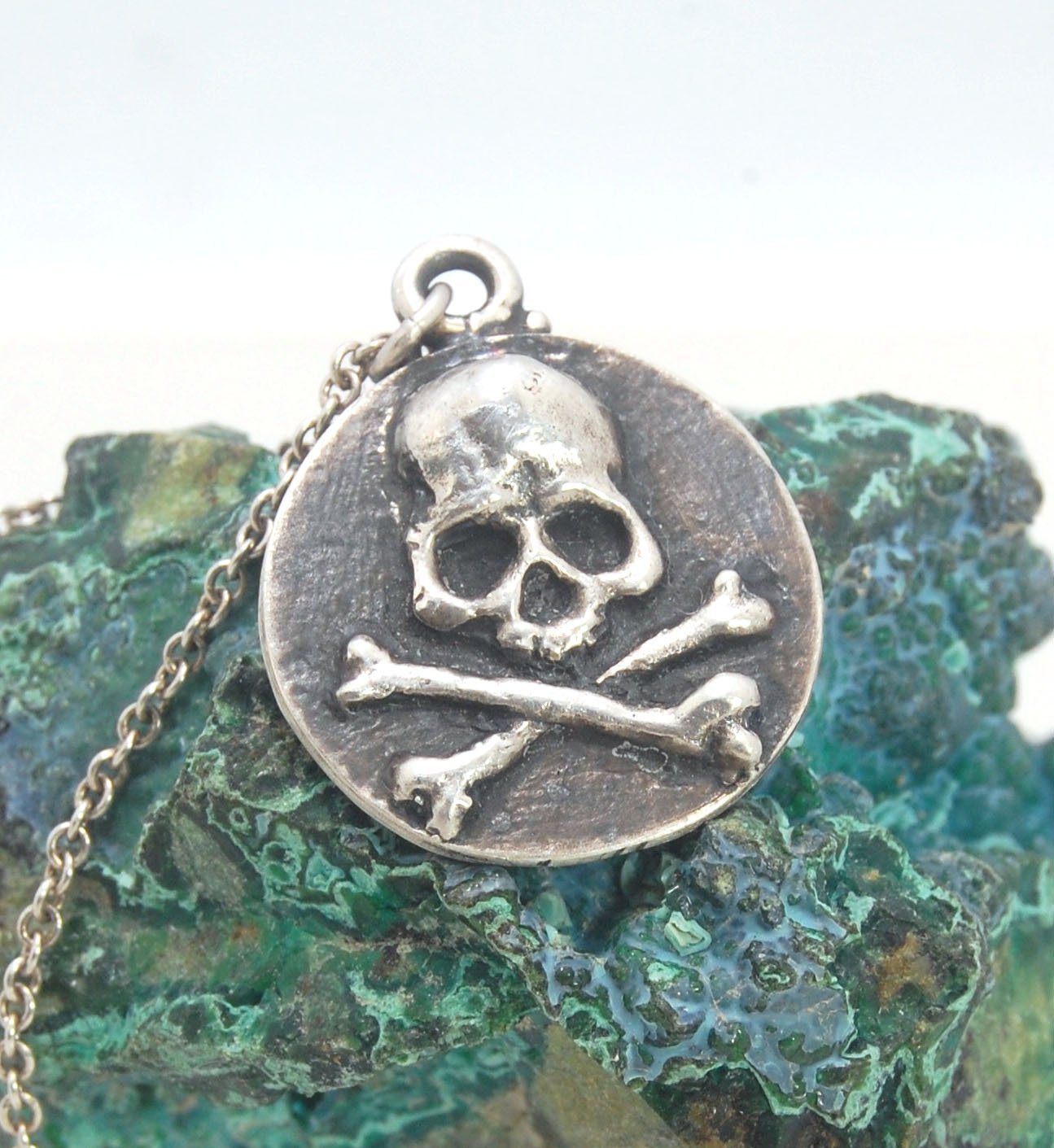 Skullbones Coin Pendant This solid sterling silver Skulbones coin pendant is wax carved by hand and cast using the ancient process of Lost Wax casting. I then made a mold, which I can inject with wax and make wax copies of the Skull and Crossbones Coin an