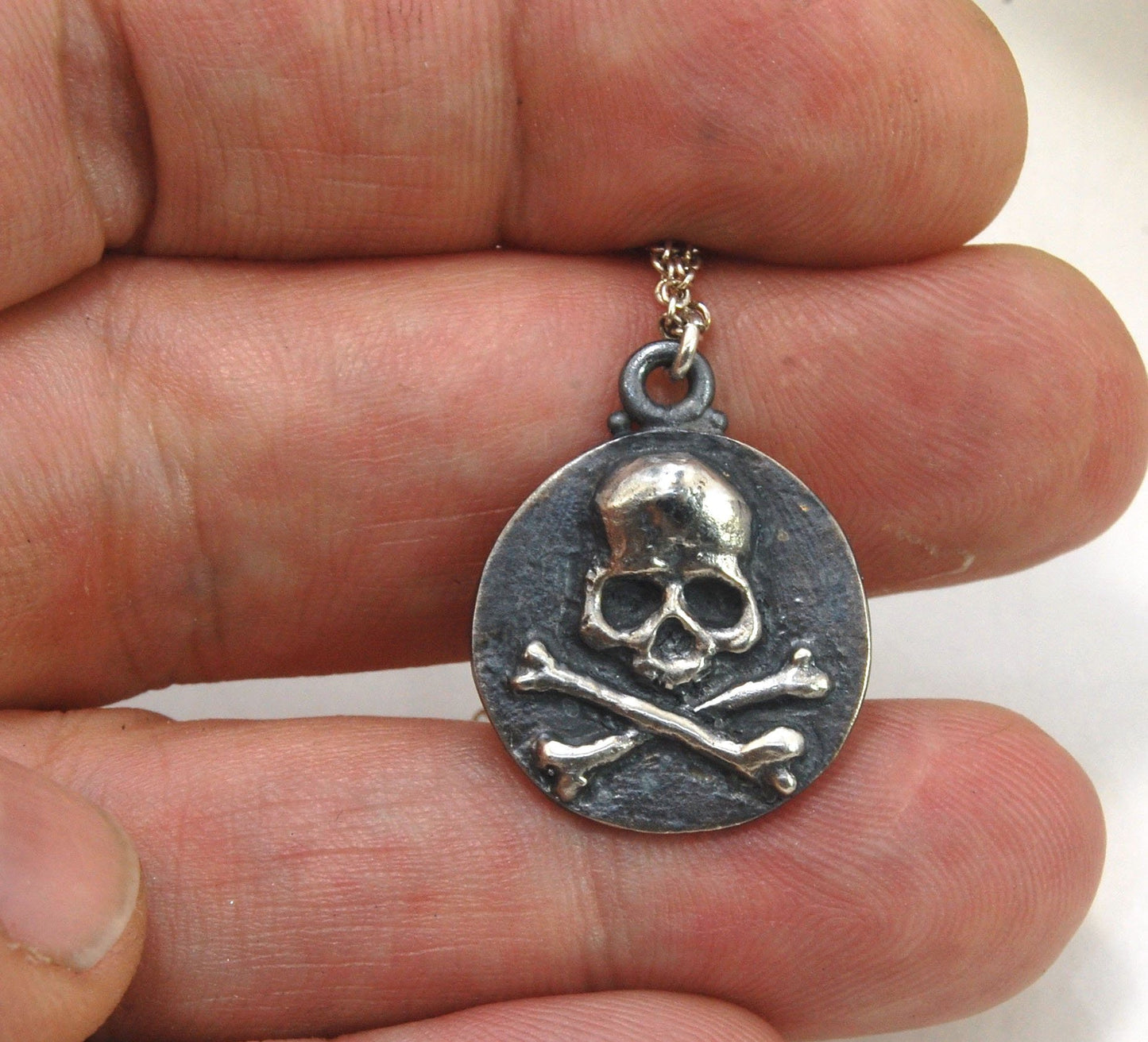 Skullbones Coin Pendant This solid sterling silver Skulbones coin pendant is wax carved by hand and cast using the ancient process of Lost Wax casting. I then made a mold, which I can inject with wax and make wax copies of the Skull and Crossbones Coin an