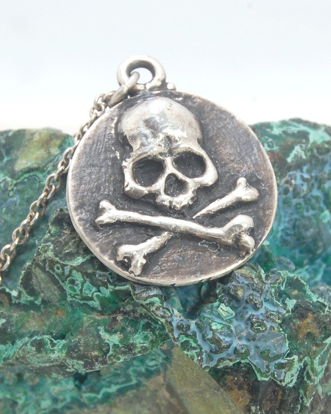 Skullbones Coin Pendant This solid sterling silver Skulbones coin pendant is wax carved by hand and cast using the ancient process of Lost Wax casting. I then made a mold, which I can inject with wax and make wax copies of the Skull and Crossbones Coin an