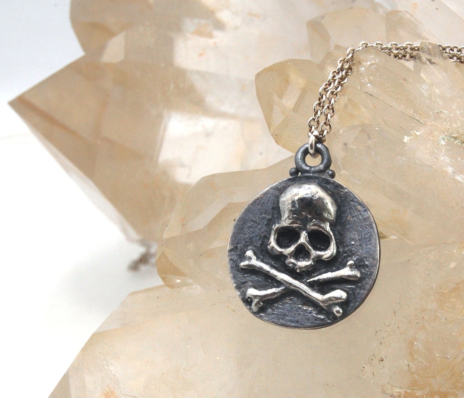 Skullbones Coin Pendant This solid sterling silver Skulbones coin pendant is wax carved by hand and cast using the ancient process of Lost Wax casting. I then made a mold, which I can inject with wax and make wax copies of the Skull and Crossbones Coin an